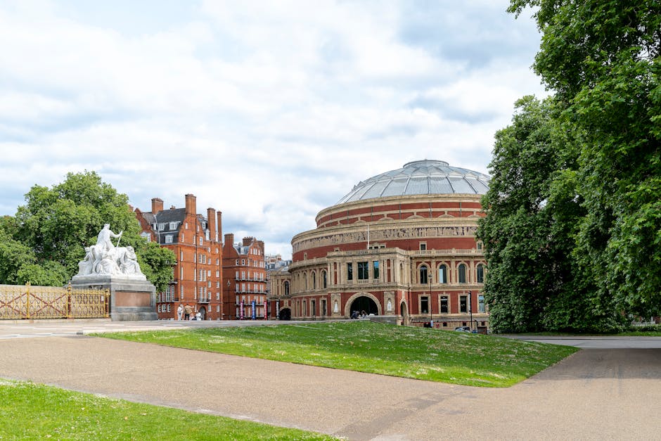 A wide view of a historic round building with a domed roof, constructed from red brick with decorative arches and large windows on the facade, situated in an outdoor setting with a paved footpath in t