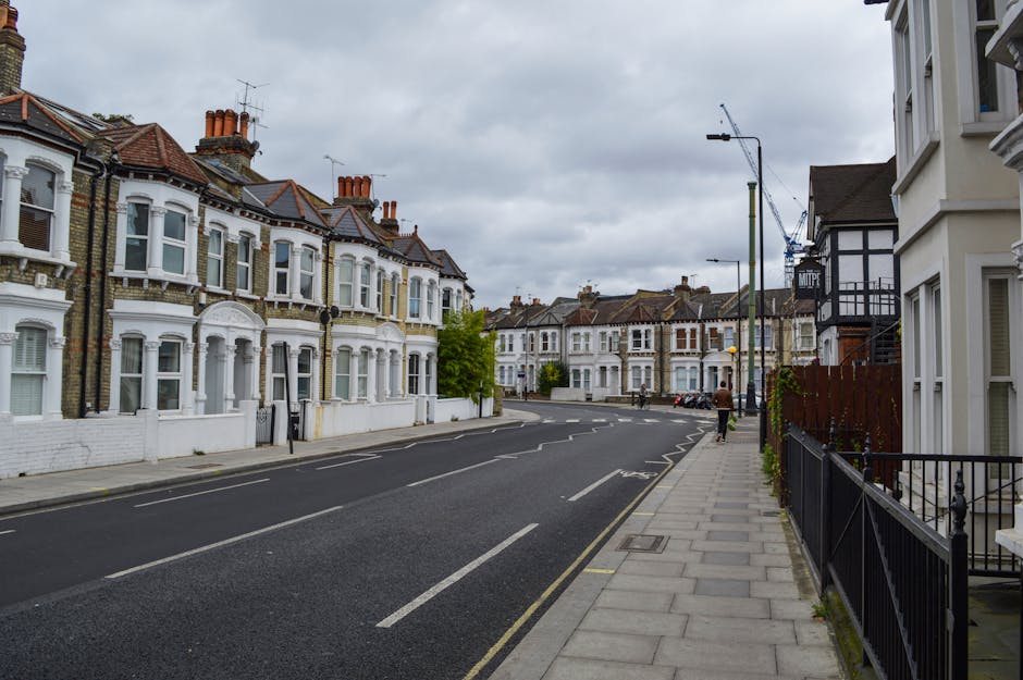 A large collection of mixed household rubbish and waste materials is piled around a metal recycling bin on a paved pavement area, with a black and a red waste disposal bin also nearby. The refuse incl